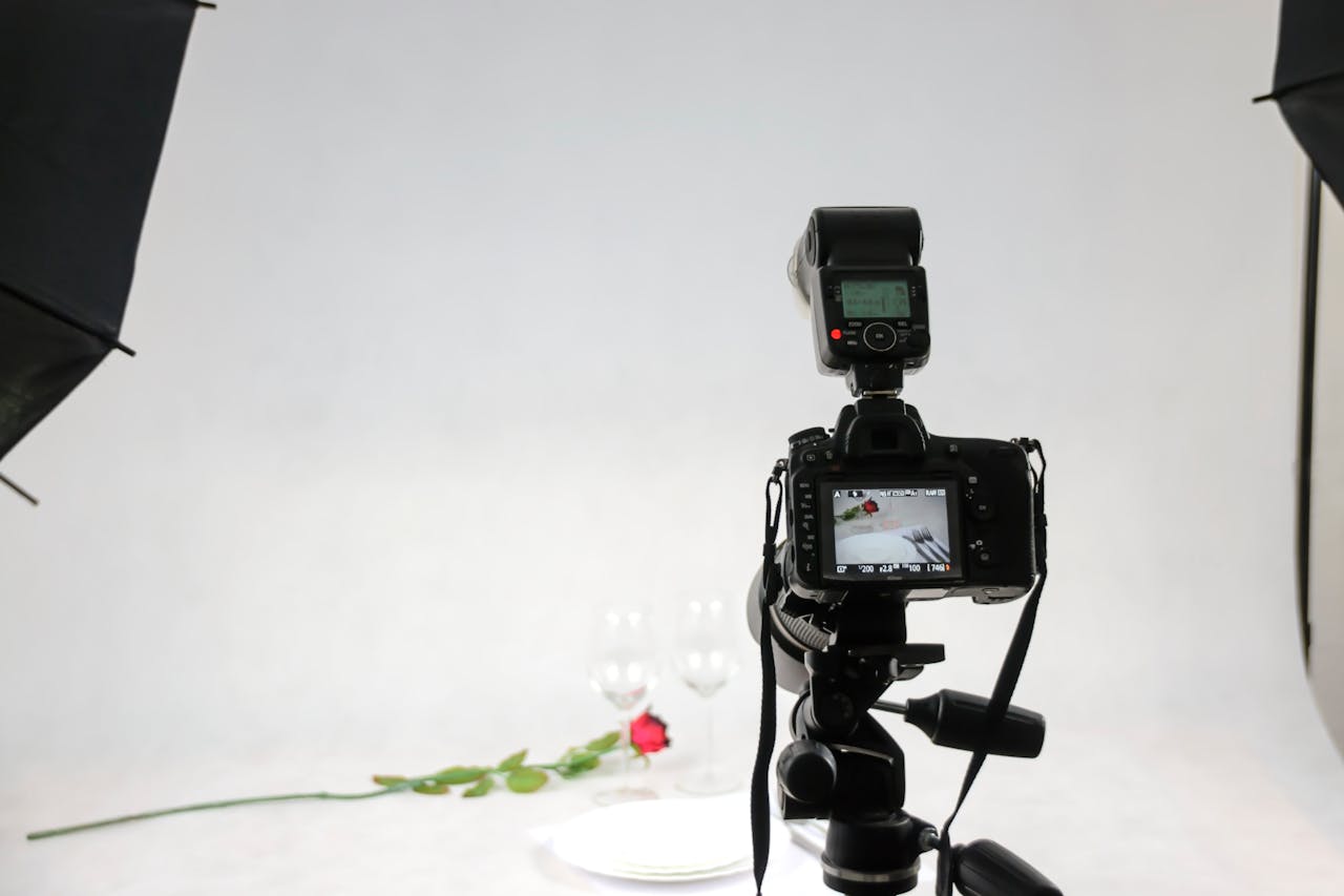 Camera setup in a photography studio capturing a rose and wine glasses.